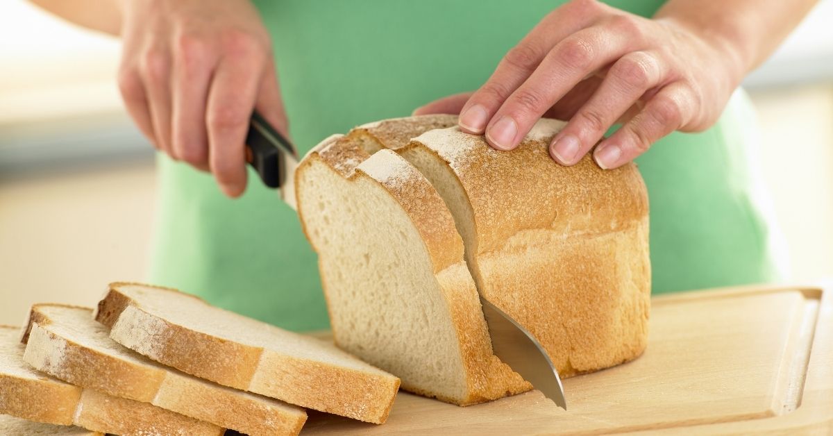 woman slicing a loaf of white bread